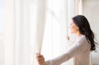 Bien-être : Femme qui ouvre un rideau devant une fenêtre